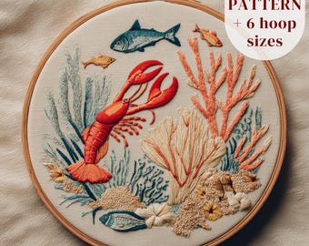 May include: Embroidered hoop art featuring an underwater scene with a red lobster, blue and orange fish, coral, and seaweed. The text "PDF PATTERN + 6 hoop sizes" is in the upper right corner. The embroidery is set in a wooden hoop.