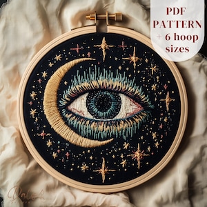 Peut inclure: Broderie dans un cercle de bois représentant un œil et un croissant de lune. Le motif comprend un œil détaillé avec un iris bleu et des accents dorés et blancs, entouré d'étoiles dorées sur fond noir. Le texte sur l'image indique "PDF PATTERN + 6 hoop sizes."