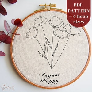 Könnte beinhalten: Eine Schwarzweiß-Zeichnung eines August-Mohnblumenstraußes in einem hölzernen Stickrahmen. Der Text "August Poppy" steht unter den Blumen.