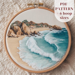 May include: An embroidery hoop containing a fabric panel with a coastal landscape scene. The design features tan cliffs, a sandy beach, and turquoise ocean waves with white foam. Text in the upper right corner reads PDF PATTERN + 6 hoop sizes.
