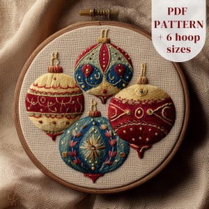 May include: Embroidered Christmas ornament pattern in a wooden hoop. The design features four colorful ornaments in red, blue, and gold. The text "PDF PATTERN + 6 hoop sizes" is visible in the upper right corner. The background is a neutral fabric.
