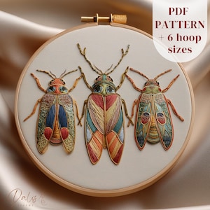 May include: An embroidered artwork in a hoop, showcasing three detailed beetles with vibrant wing patterns. The insects are stitched with shades of orange, blue, green, and red. The text "PDF PATTERN + 6 hoop sizes" is displayed. The piece is set within a wooden embroidery hoop.