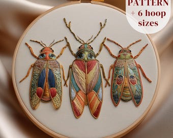 May include: Embroidered hoop art featuring three colorful beetles with detailed wing patterns. The insects are stitched with various colors, including orange, blue, green, and red. The text "PDF PATTERN + 6 hoop sizes" is visible. The artwork is set in a wooden embroidery hoop.