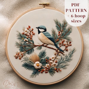 May include: Embroidered hoop art featuring a blue, black, and beige bird perched on a branch surrounded by greenery and berries. The design is set against a cream-colored fabric within a wooden hoop. Text on the upper right says "PDF PATTERN + 6 hoop sizes."