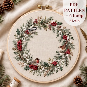 May include: An embroidery hoop containing a fabric panel with a stitched wreath design featuring green pine branches, red berries, white berries, and three small birds. The text PDF PATTERN + 6 hoop sizes is printed in the upper right corner.