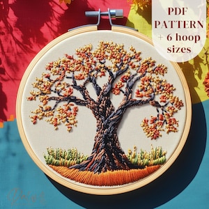 May include: An embroidered tree design in a wooden hoop. The tree has orange, yellow, and brown leaves, with a dark blue and brown trunk and branches. Text reads "PDF PATTERN + 6 hoop sizes".