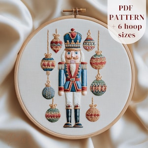 May include: Embroidered Christmas ornament pattern featuring a nutcracker soldier and hanging ornaments in a wooden hoop. The nutcracker is in a blue and red uniform. The text "PDF PATTERN + 6 hoop sizes" is visible.