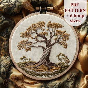 May include: An embroidered tree design in a wooden hoop. The tree features a twisted trunk and detailed branches with golden-brown leaves. The text "PDF PATTERN + 6 hoop sizes" is visible. The background is a cream-colored fabric.