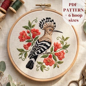May include: A round wooden embroidery hoop containing a fabric panel with a stitched hoopoe bird featuring a crest, black and white wing feathers, and a long beak, surrounded by embroidered red flowers and green leaves. Text reads PDF PATTERN + 6 hoop sizes.