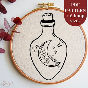 May include: A black and white line drawing of a bottle with a crescent moon and stars inside. The bottle is in a wooden embroidery hoop. The text "PDF PATTERN + 6 hoop sizes" is in the upper right corner of the image.