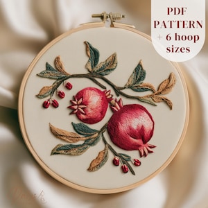 Peut inclure: Broderie d'un motif de grenade dans un cercle en bois. L'œuvre présente deux grenades rouges avec des feuilles vertes et marron et de petites baies rouges. Le texte "PDF PATTERN + 6 hoop sizes" est en haut à droite.