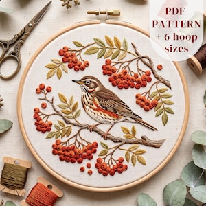 Puede incluir: Un bastidor de bordado que contiene un panel de tela con un diseño bordado de un pájaro marrón y blanco posado en una rama rodeado de racimos de bayas rojas y hojas verdes. El texto en la imagen dice: PDF PATTERN + 6 hoop sizes.