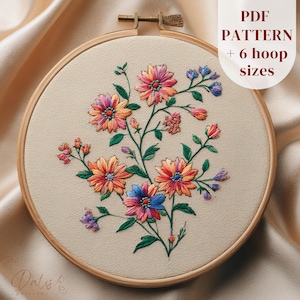 以下が含まれることがあります： 木製のフレームに入った花の刺繍デザイン。ピンク、オレンジ、青の色合いのカラフルな花と緑の葉が特徴です。「PDF PATTERN + 6 hoop sizes」の文字が右側に表示されています。