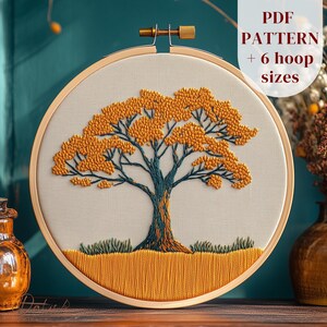Puede incluir: Diseño de árbol bordado en un aro de madera. El árbol presenta un tronco marrón, ramas verde azulado y hojas de color amarillo dorado. El texto "PDF PATTERN + 6 hoop sizes" es visible en el lado derecho del aro.