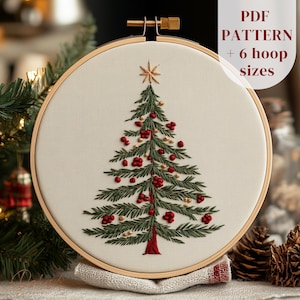 Può includere: Ricamo di un albero di Natale in un telaio di legno. L'albero è verde con accenti di bacche rosse e una stella dorata in cima. Il testo "PDF PATTERN + 6 hoop sizes" è visibile.