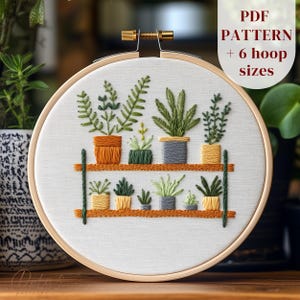 以下が含まれることがあります： 棚に鉢植えの植物が置かれたデジタル刺繍パターン。パターンには6つのフープサイズが含まれており、PDFダウンロードとして入手できます。植物はさまざまな緑色で、鉢はオレンジ、イエロー、グレーです。