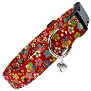 May include: Red dog collar featuring a floral pattern in yellow, blue, pink, and green. The collar has a silver metal D-ring and a heart-shaped charm with "Best Friend". It has a black plastic buckle.