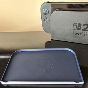 May include: A dark grey Nintendo Switch console and a matching dark blue tray. The console has the text "Nintendo Switch" printed on it. The tray is rectangular with rounded corners.