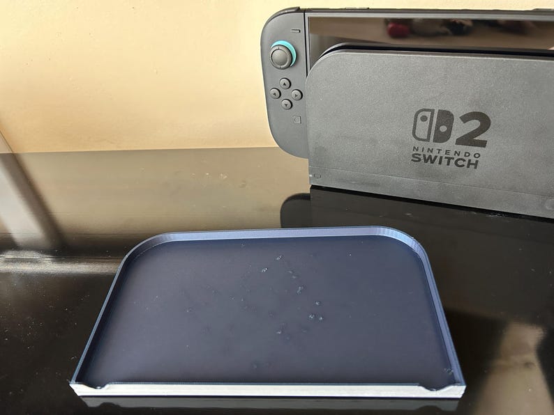 May include: A dark grey Nintendo Switch console and a matching dark blue tray. The console has the text "Nintendo Switch" printed on it. The tray is rectangular with rounded corners.