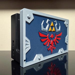 May include: A 3D-printed shield with a blue background, red bird emblem, and yellow and white symbols. The shield has a silver frame and is mounted on a black rectangular base.