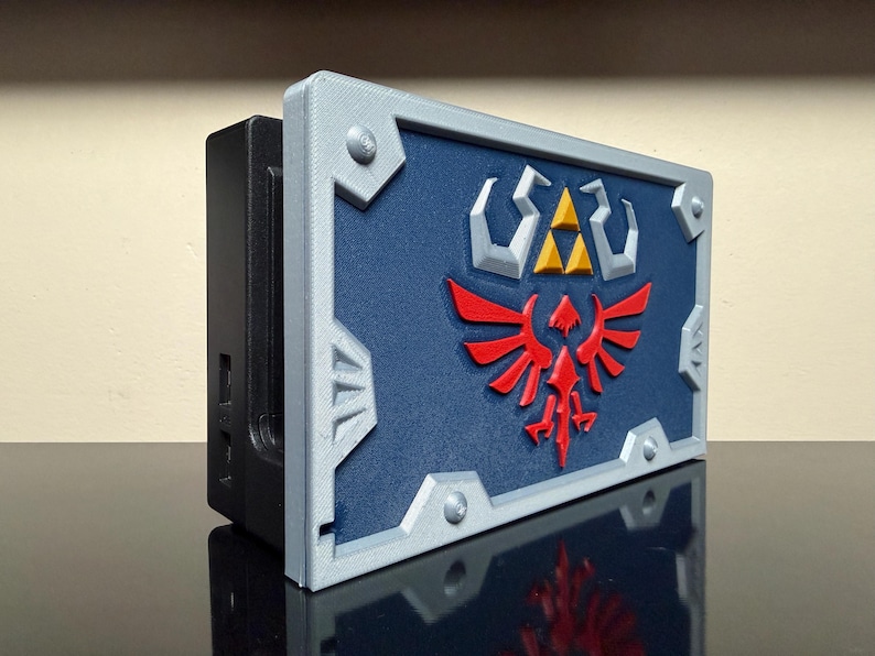 May include: A 3D-printed shield with a blue background, red bird emblem, and yellow and white symbols. The shield has a silver frame and is mounted on a black rectangular base.