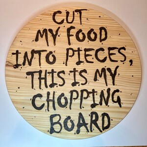 May include: A round wooden chopping board with the text "Cut my food into pieces, this is my chopping board" burnt into the surface.