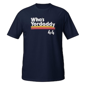 Könnte beinhalten: Marineblaues T-Shirt mit einer Retro-Grafik, die "Who's Yordaddy 44" in weißer Schrift mit einem roten, orangefarbenen und gelben Streifenmuster zeigt.