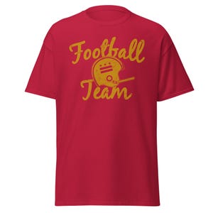 May include: Red t-shirt with a gold graphic of a football helmet and the text "Football Team".
