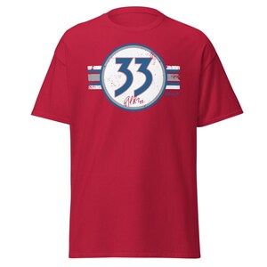 May include: Red t-shirt featuring a white circle with the number 33 in blue, giving a distressed effect. The circle has a grey border and is surrounded by three blue and white stripes. The text "Alkins" is written in blue below the number.