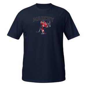 May include: A navy blue t-shirt with a graphic of a hockey player in a red and white jersey with the text "MARCHY" above the player.
