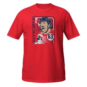 May include: Red t-shirt with a graphic of Brad Marchand, a hockey player wearing a red and white jersey with the number 63 on it. The text "Brad Marchand" is printed vertically on the left side of the graphic.