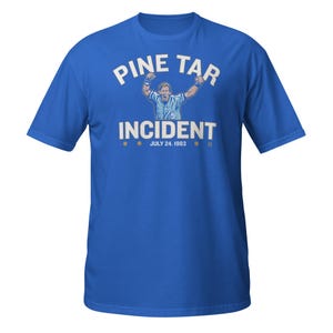 Può includere: Una t-shirt blu reale con testo bianco che recita "Pine Tar Incident" e "July 24, 1983". Un'immagine di un giocatore di baseball in stile cartone animato con le braccia alzate in segno di vittoria si trova al centro della t-shirt.