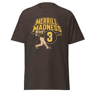 Puede incluir: Camiseta marrón con un gráfico amarillo de un jugador de béisbol balanceando un bate. El gráfico dice "Merrill Madness 3".