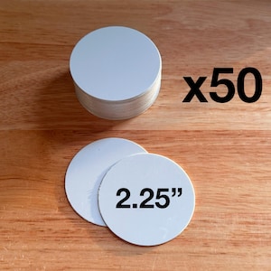 May include: A stack of fifty white circular discs, each measuring 2.25 inches in diameter. The set includes a large pile of these blank round items, with two individual discs placed in front showing the size text 2.25 inches clearly.