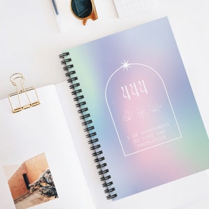 May include: A spiral bound notebook with a holographic cover featuring the number 444 and the text "I am surrounded by love and protection".