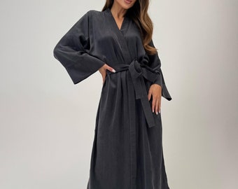 May include: A dark gray, knee-length robe with wide sleeves and a matching belt. The robe is made of a soft, flowing fabric. The model is wearing silver strappy heels.