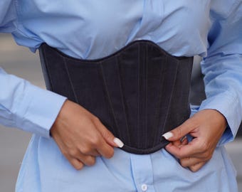 Puede incluir: Un corsé gris oscuro con costuras verticales. Se lleva sobre una camisa azul claro y se combina con una falda plisada a cuadros. El conjunto mezcla estilos clásicos y modernos.