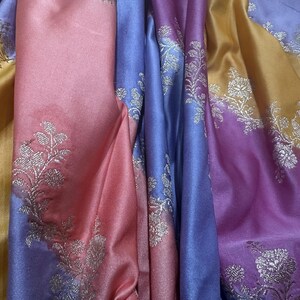 May include: Close-up of colorful fabric with a floral design. The fabric is a mix of gold, pink, purple, and blue. The floral pattern is in silver. The fabric has a shiny, silky appearance.