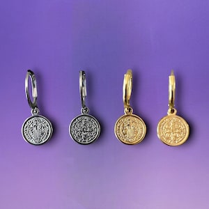 May include: Four pairs of hoop earrings with a Saint Benedict medal pendant. The medals are silver, gold, and two different shades of gold.
