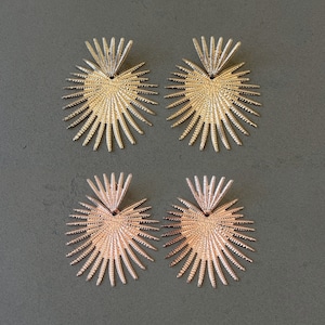 May include: A pair of gold heart-shaped earrings with a sunburst design and a pair of rose gold heart-shaped earrings with a sunburst design.