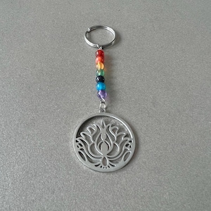 May include: A silver key chain with a circular charm featuring a detailed lotus flower design. The chain is adorned with a rainbow of colorful beads.