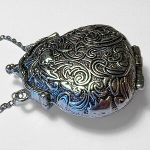 Puede incluir: Un collar con un medall&oacute;n de plata con un dise&ntilde;o floral ornamentado. El medall&oacute;n tiene forma de coraz&oacute;n y tiene un cierre con bisagra.