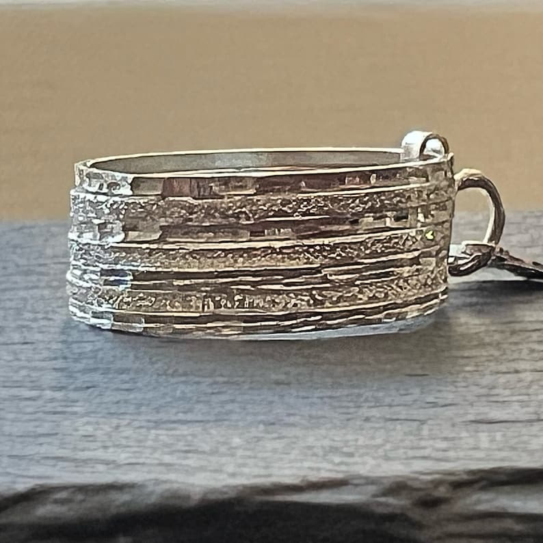 May include: A silver ring with a textured, layered design. The ring has a unique, organic shape and a hammered finish.