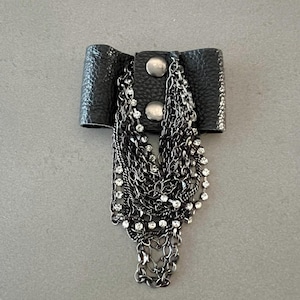 May include: Black leather cuff bracelet with silver-tone metal accents and multiple strands of dangling chains adorned with clear rhinestones. The bracelet is secured with two silver-tone metal buttons.