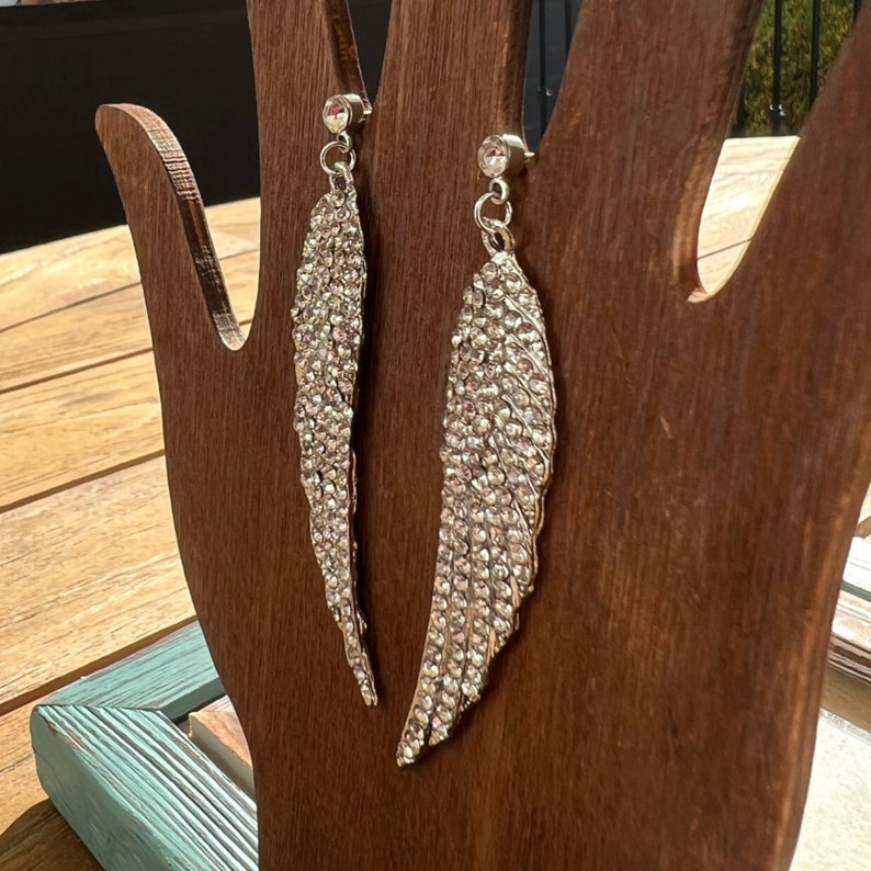 May include: A pair of silver dangle earrings with a wing design. The wings are covered in clear rhinestones.