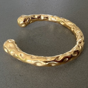 May include: A gold-toned hammered metal bangle bracelet with a textured surface.