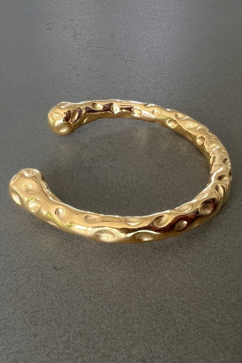 May include: A gold-toned hammered metal bangle bracelet with a textured surface.