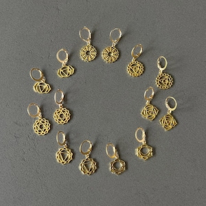 Könnte beinhalten: Ein Set mit zehn goldfarbenen Ohrringen mit verschiedenen Chakra-Symbolen. Jeder Ohrring hat einen kleinen Ring und einen Anhänger mit einem einzigartigen Design.