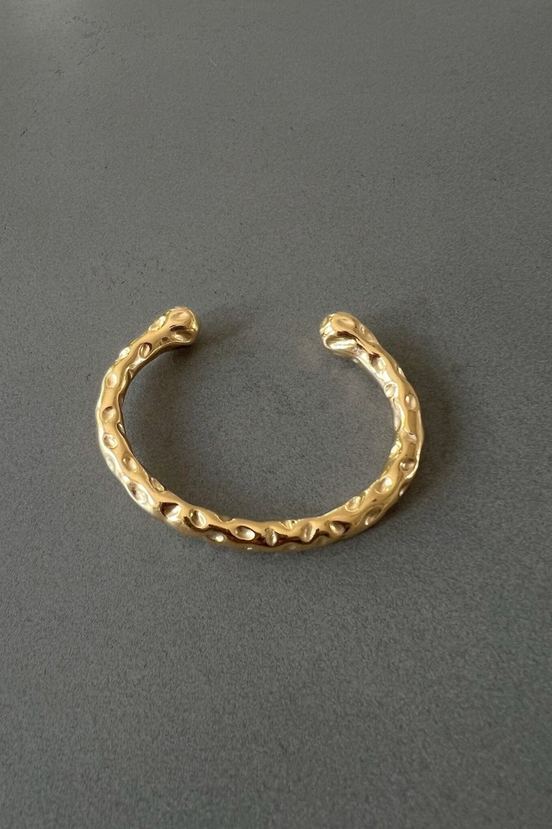 May include: A gold-toned textured bangle bracelet with a hammered finish.