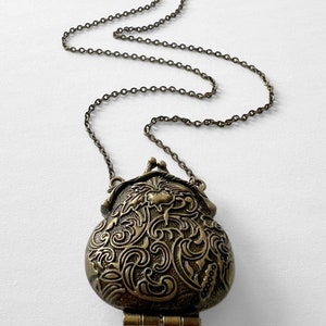 Puede incluir: Un collar dorado con un colgante de medall&oacute;n detallado, adornado y con bisagras. El medall&oacute;n tiene forma de bolsa y presenta un dise&ntilde;o floral.